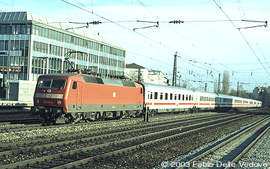 Die verkehrsrote 120 114-4 schiebt den IR 2097 (München Hbf 15:37 - Salzburg Hbf 17:23) durch den Bahnhof Heimeranplatz (München, Frühling 2002).