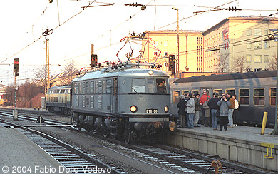 Die Altbauellok wird schon sehnsüchtig von den Eisenbahnenthusiasten erwartet. Der abfahrende Nahverkehrszug im Hintergrund mit seiner oceanblau-beigen 218 und den Silberlingen ist auch schon lange Geschichte (München Hauptbahnhof, 1990).