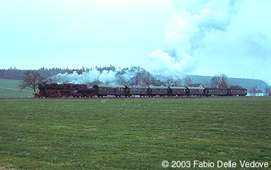Zum Vergrößern klicken - Bei leichtem Schneetreiben kommt die 52 7596 mit ihren 7 Wagen aus Bad Wurzach (Mennisweiler, 06. April 2003).